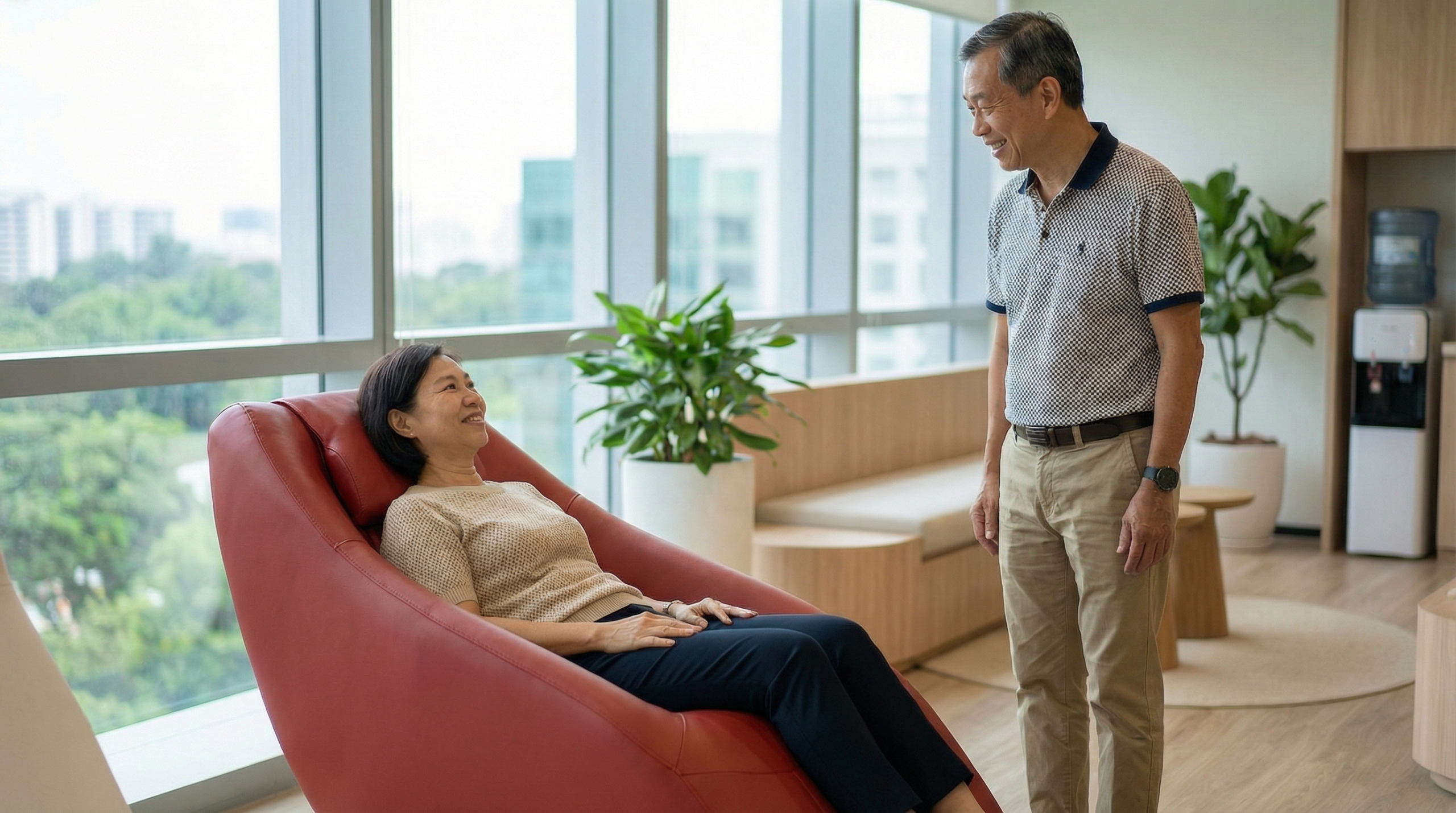 Older Singaporean employees in their 50s trying whole body vibration wellness chair in a modern Singapore office wellness room during work break โ corporate passive exercise MSK solution